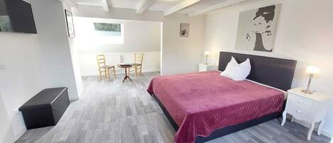 A modern bedroom with a large bed, a small table with chairs, a nightstand, and a painting on the wall.