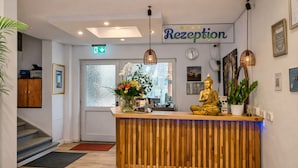 A reception area with a wooden reception desk, a Buddha statue, and a sign that reads "Reception". - SILONCE Hotels & Restaurant (Radevormwald)