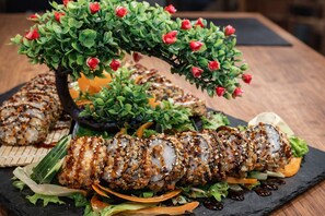 Un plateau de sushis avec différents types de maki et une plante décorative aux fleurs rouges.