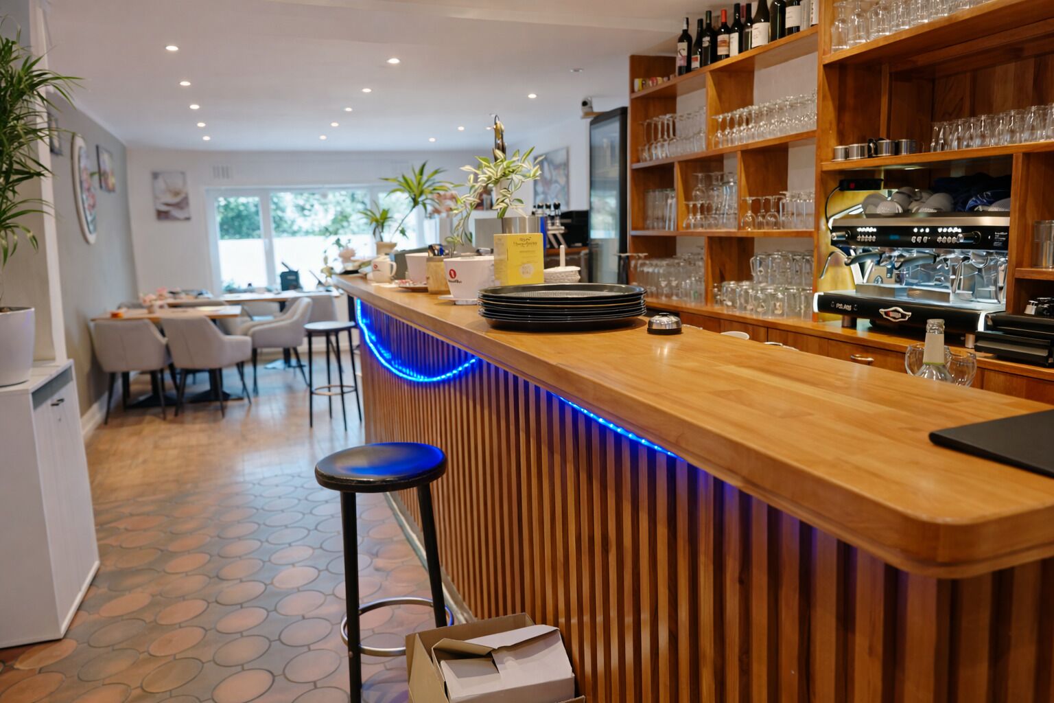 Una zona de bar moderna con mostrador de madera, taburetes y una estantería para vinos.