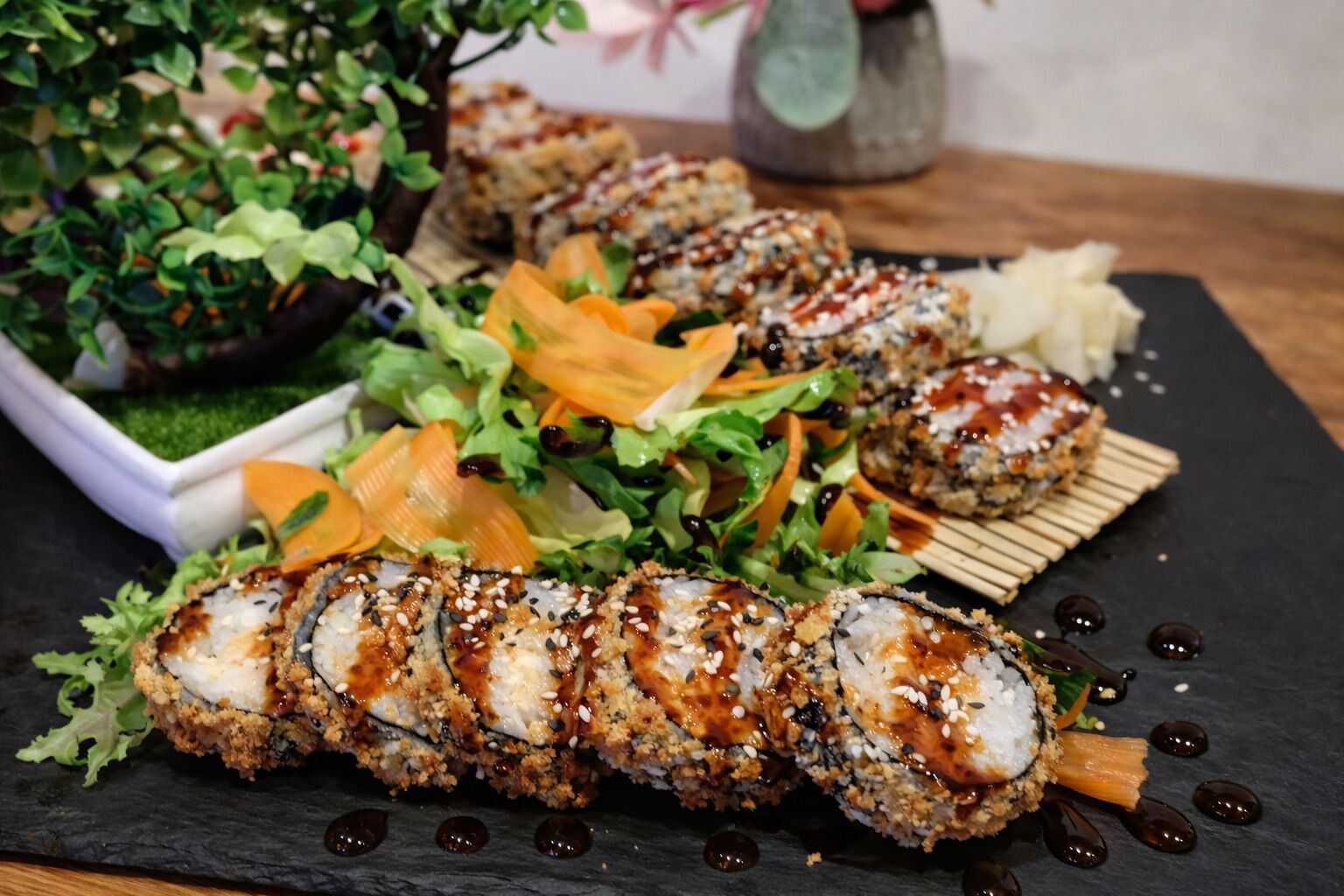 A sushi platter with various rolls and a side salad, set on a slate board.