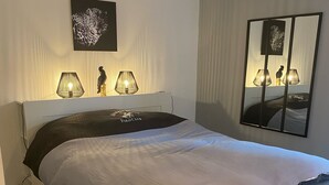 A modern bedroom with a white bed, grey bedding, two wall-mounted lamps, a leopard print artwork, and a mirror reflecting the bed. - Exceptional sea view apartment (Cerbère)