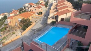 A rooftop swimming pool with a wooden deck, surrounded by terraced buildings with red roofs, overlooking a coastal area. - Exceptional sea view apartment (Cerbère)