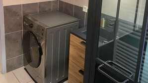 A compact kitchen with a built-in washer and dryer, a small countertop, and a glass door leading to a bathroom. - Exceptional sea view apartment (Cerbère)