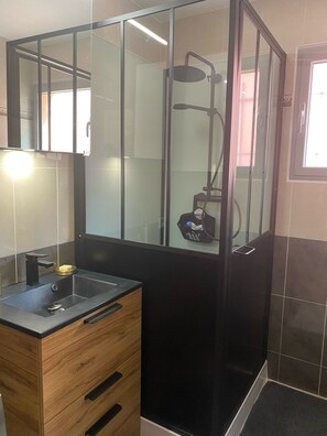A modern bathroom with a glass-enclosed shower, a wooden vanity with a sink, and a mirror.