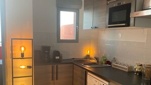 A compact kitchen with wooden cabinets, a dishwasher, a microwave, and a built-in oven. - Exceptional sea view apartment (Cerbère)