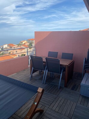 A balcony with a wooden table and chairs, a view of the cityscape, and a pink wall.