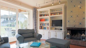 A living room with a sofa, a glass coffee table with a book, a fireplace, and a bookshelf. - House (Wenningstedt)