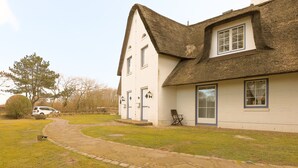 A white house with a thatched roof, a stone pathway, and a parked car. - House (Wenningstedt)
