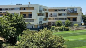 A multi-story residential building with balconies and a sports field in the foreground.