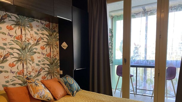 A bedroom with a bed, pillows, a nightstand, and a window with a view of the outside.