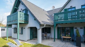 Ein zweistöckiges Haus mit Balkon, einer Terrasse und Sitzgelegenheiten sowie einer Satellitenschüssel.