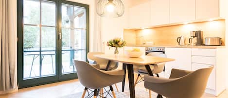 A modern kitchen with white cabinets, a dining table with four chairs, and a large window with a view of the outdoors.