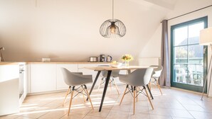 A modern kitchen with a dining area, featuring a large window, a hanging light fixture, and a view of the outdoors. - Upper floor apartment Lee West 2.3 (Ostseebad Dierhagen)