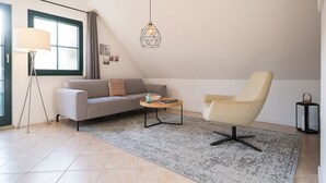 A modern living room with a sofa, armchair, and a small table with a lamp and decorative items. - Upper floor apartment Lee West 2.3 (Ostseebad Dierhagen)