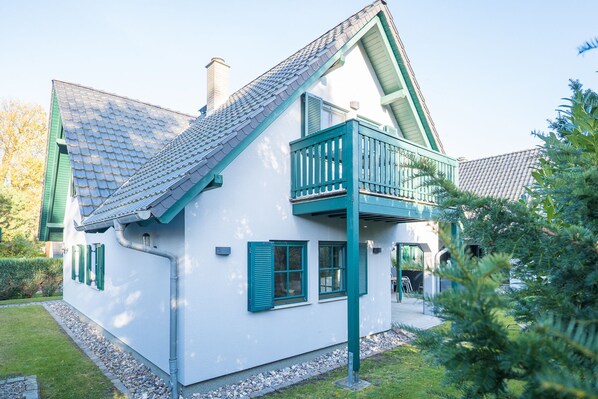 A white house with green shutters, a balcony, and a sloped roof.