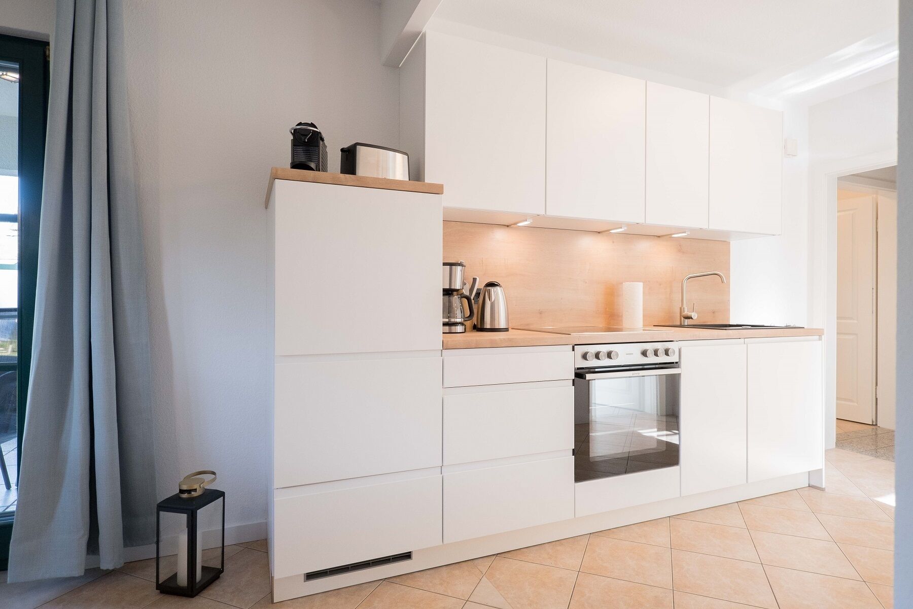 A modern kitchen with white cabinetry, a built-in oven, and a stainless steel sink.