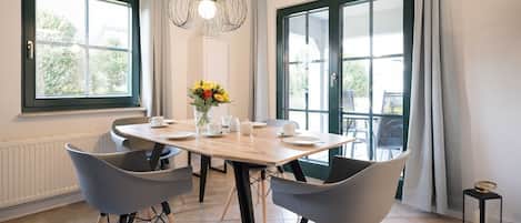 A dining area with a wooden table, four grey chairs, a vase with yellow flowers, and a hanging light fixture.
