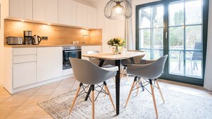 Una cocina moderna con armarios blancos, horno integrado y cafetera. Hay una mesa de comedor con cuatro sillas y un florero con flores.
