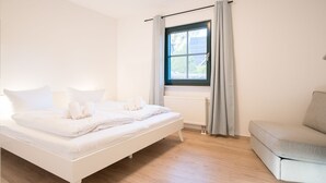 Un dormitorio con cama, ventana con cortinas, radiador y sofá.