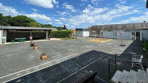 Ein Parkplatz mit Basketballfeld, grünen Stühlen und einer überdachten Sitzgelegenheit.