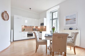 Una cocina moderna con armarios blancos, un comedor con mesa y sillas, y un amplio ventanal que proporciona luz natural.