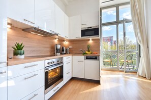 Eine moderne Küche mit weißen Schränken, einem eingebauten Backofen und einem großen Fenster mit Blick auf einen Balkon.