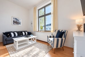 Ein modernes Wohnzimmer mit einer Couch, einem Sessel, einem Couchtisch und einem Fenster mit Vorhängen.