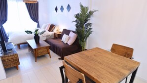 A cozy living room with a sofa, a wooden dining table, and a coffee table. There is a potted plant and a lamp on the table. - Mishuku Onna102 (Onna)