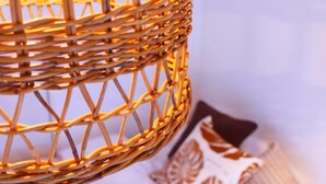 A close-up of a woven wicker lamp with a warm glow, set against a soft background with patterned cushions. - Mishuku Onna102 (Onna)