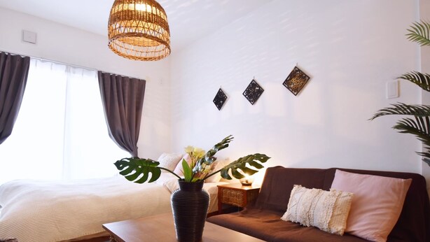 A modern bedroom with a bed, a wooden table with a vase of flowers, a brown sofa, and a hanging light fixture. - Mishuku Onna102 (Onna)