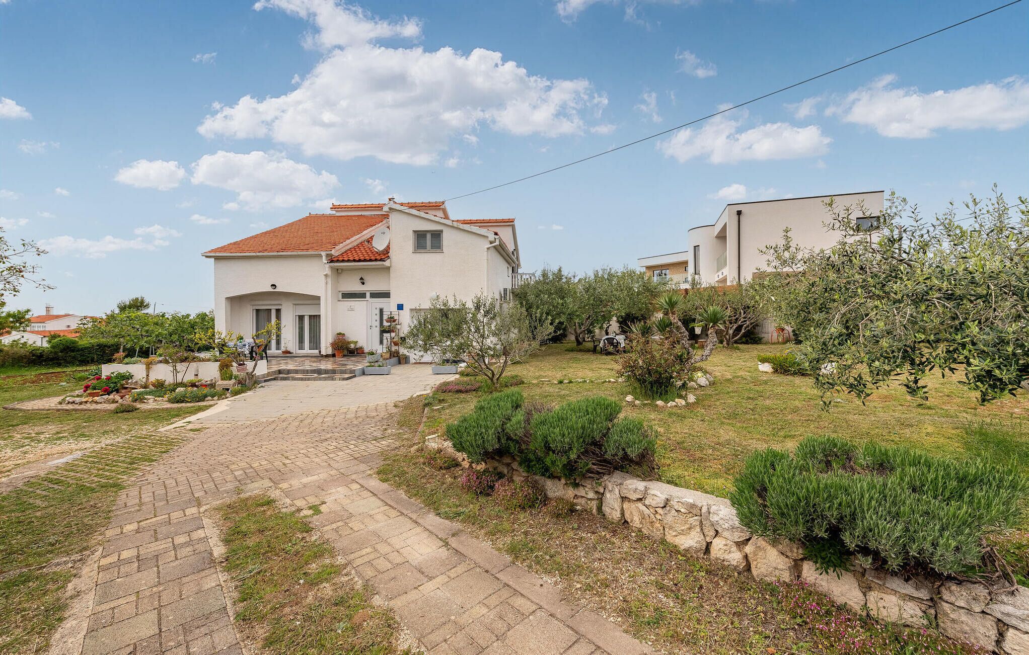 Ein zweistöckiges Haus mit rotem Ziegeldach, einem gepflasterten Einfahrt und einem Garten mit verschiedenen Pflanzen und Sträuchern.