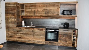 A kitchen with wooden cabinetry, a built-in microwave, a stove, and a coffee maker. - Cozy holiday chalet with top facilities - Hausen on the ground floor - near Chiemsee (Pittenhart)