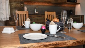 A dining table set with white plates, cutlery, and glasses, with a loaf of bread and a bowl of fruit on the table. - Cozy holiday chalet with top facilities - Hausen on the ground floor - near Chiemsee (Pittenhart)