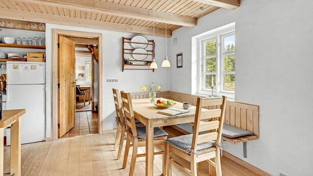 Una cocina acogedora con vigas de madera, una mesa de comedor con sillas y una ventana con vistas a árboles.