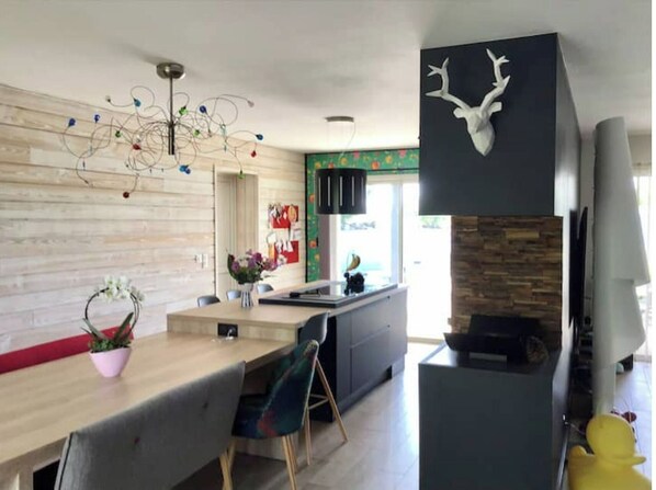 Una cocina moderna con encimera de madera, un comedor con mesa y sillas, una pared decorativa con cabeza de ciervo y una chimenea de piedra.