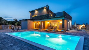 Une maison moderne à deux étages dotée d’une piscine, d’un espace salon extérieur et d’un coin barbecue.