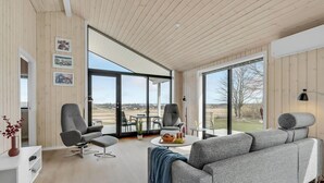 Una sala de estar moderna con un sofá gris, dos sillones, una mesa de centro y vistas al exterior a través de grandes puertas corredizas de vidrio.