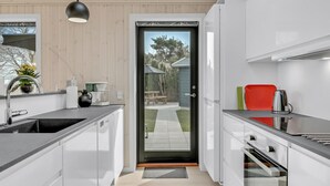 Una cocina moderna con armarios blancos, una lámpara colgante negra y vistas a un patio exterior a través de un ventanal.