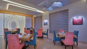 Un restaurante con mesas dispuestas para comer, con una decoración moderna que incluye iluminación decorativa y obras de arte en las paredes.