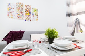 A dining table set with plates, glasses, and cutlery, a small plant, and a purple throw on a grey sofa.