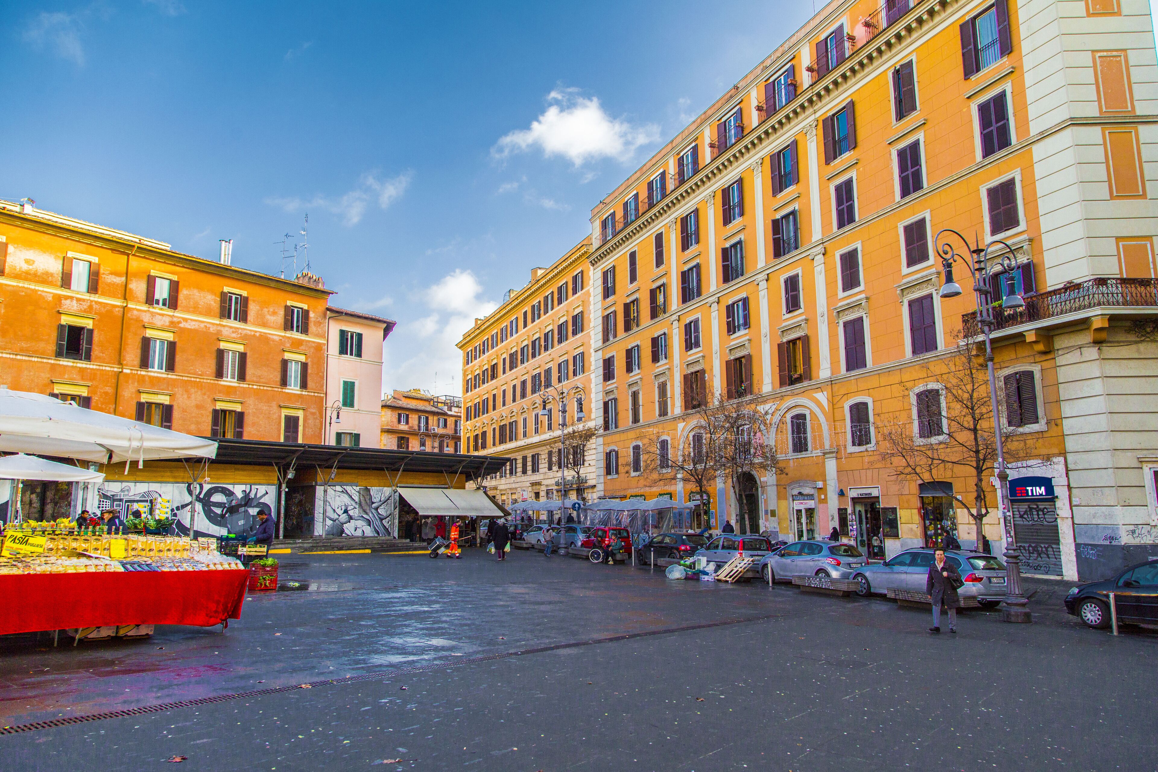 A street with parked cars and a market stall.