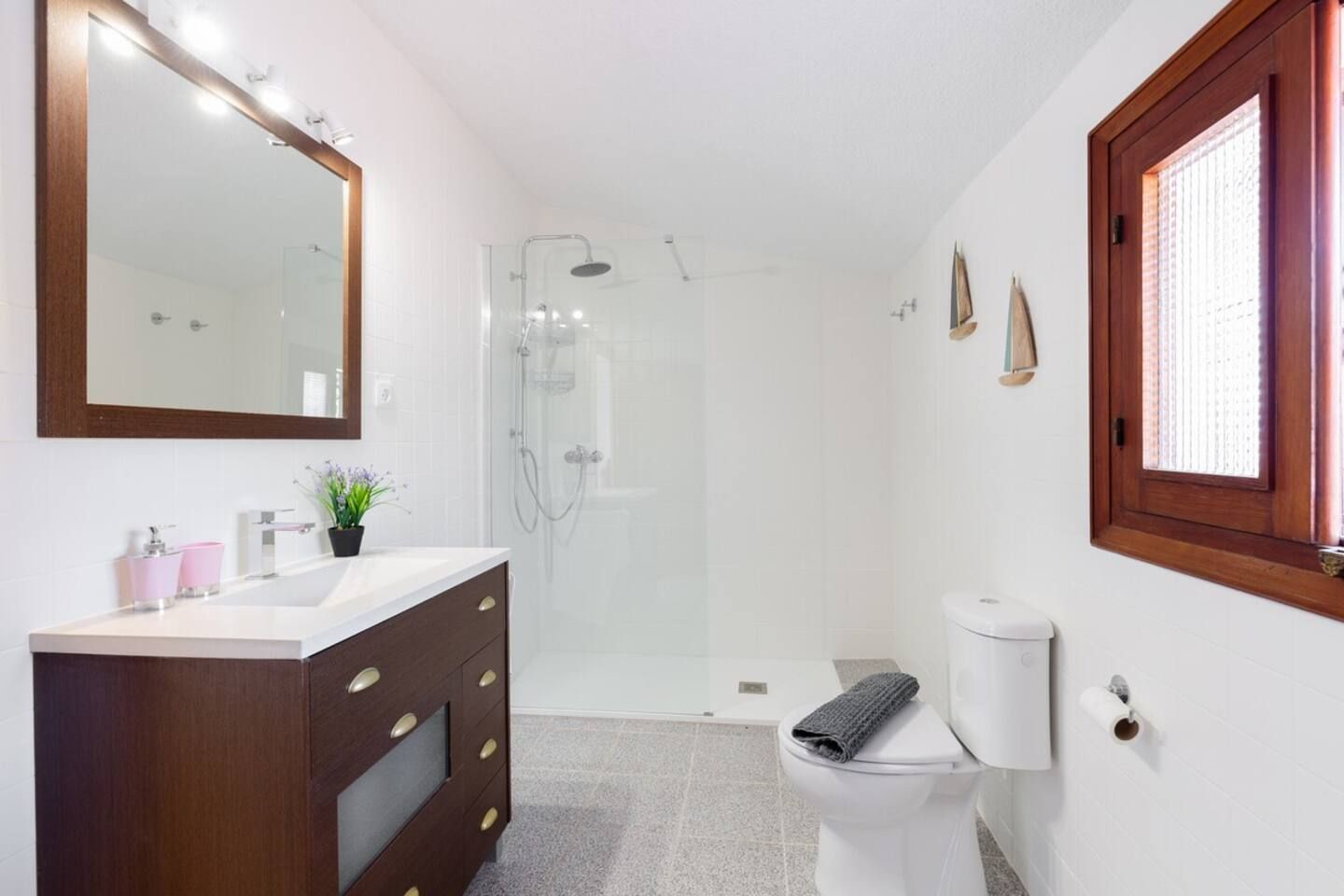Une salle de bain comprenant une douche, des toilettes, un meuble-lavabo avec des tiroirs, un miroir et une fenêtre.