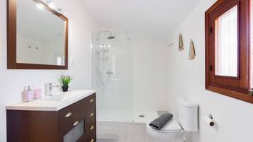 Une salle de bain comprenant une douche, des toilettes, un meuble-lavabo avec des tiroirs, un miroir et une fenêtre.