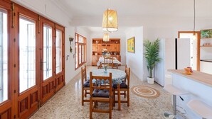 Une cuisine spacieuse avec des meubles en bois, une table à manger avec des chaises, un luminaire suspendu et une plante en pot.