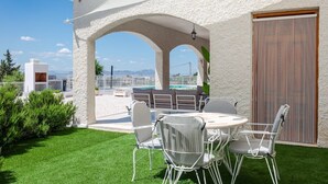 Une terrasse avec une table et des chaises blanches, une vue sur la mer et un bâtiment à la façade blanche.