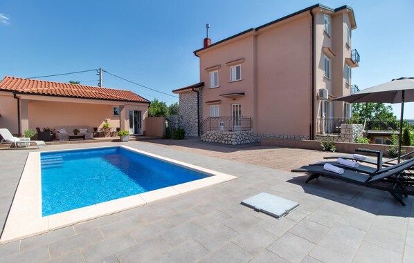 Piscina con sillones de descanso y un patio cubierto.