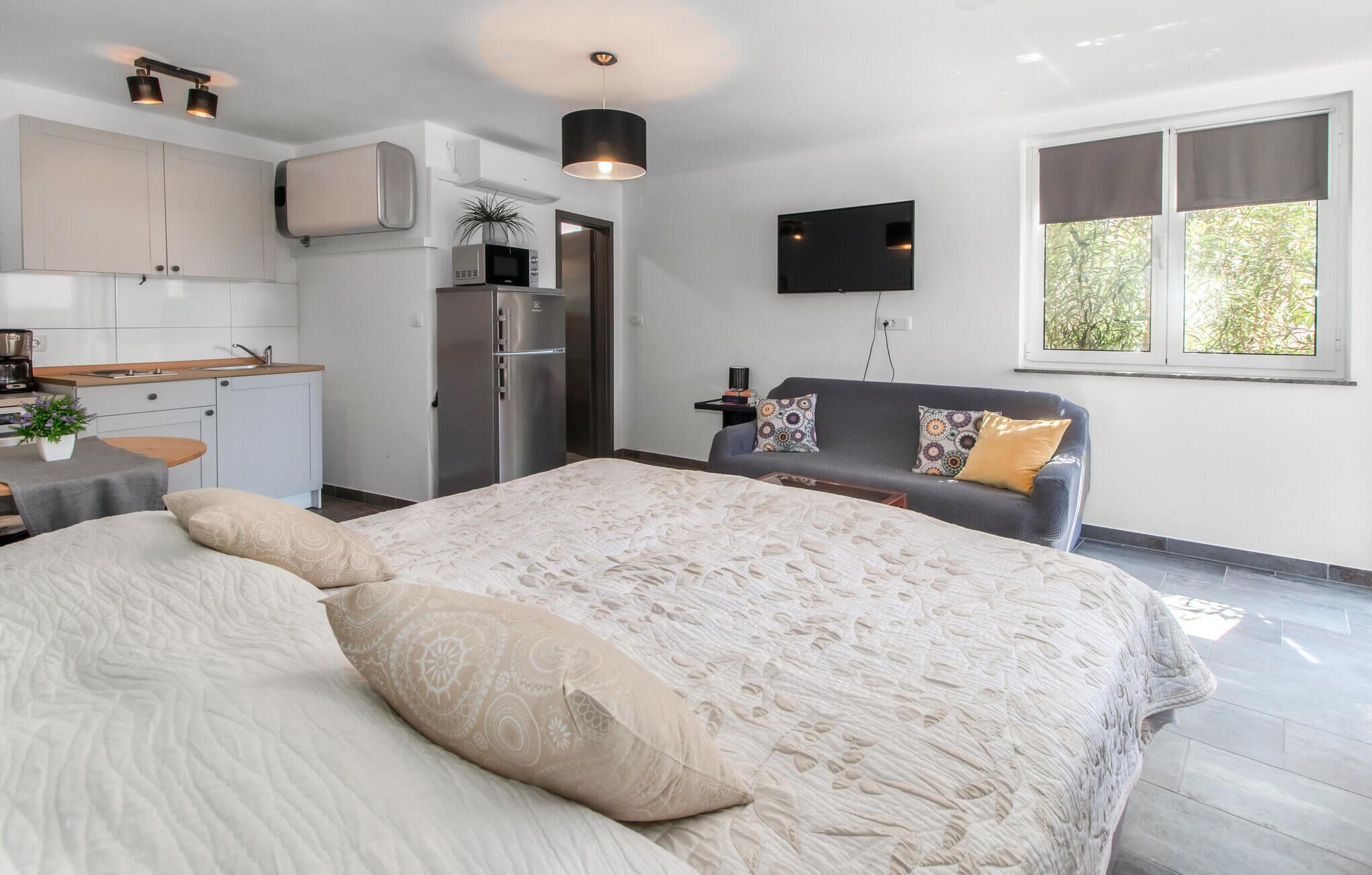 A modern bedroom with a large bed, a sofa, a TV, and a kitchen area.