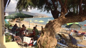 Un café situé en bord de mer, avec une terrasse, des parasols et une vue sur l’océan.