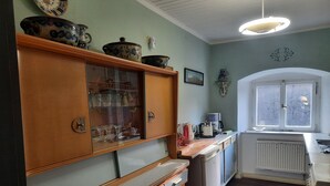 A kitchen with wooden cabinets, a refrigerator, and a window with a view. - Living in a stately home from 1848 in the Fichtelgebirge (Ebnath)
